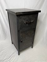 Front view of the industrial-style metal side table showing closed drawer and cabinet door with leather handles.