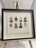 Full view of the framed print showing nine illustrated women wearing headsets, matted and in black frame on an easel.