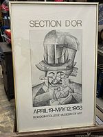 Straight-on photo of the framed black and white cubist poster showing the geometric man wearing an opera hat with exhibition information.