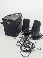 Photo of two Logitech R-20 desktop satellite speakers with cables and a subwoofer unit, black finish, placed against a white background.