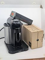 Front and side angle showing Breville Nespresso VertuoPlus coffee maker with the crate and sealed box of decaf pods