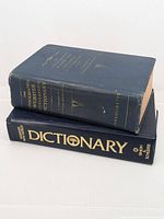 Two hardcover Webster's dictionaries stacked, showing spine and wear on the older 1959 edition and pristine condition on the 1991 Simon & Schuster edition.
