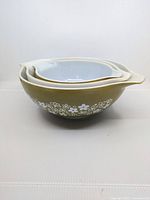 Stacked nesting Pyrex Cinderella bowls, showing olive green exterior with white floral Spring Blossom pattern and white interior.