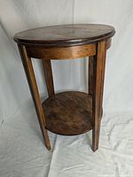 Full view of the solid wood side table showing round top and lower shelf with three legs.