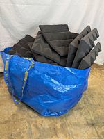 Large blue bag filled with multiple black pyramid-shaped acoustic foam panels stacked inside.