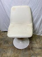 Front view of white Tulip chair showing flaking upholstery and solid metal pedestal base on concrete floor with white backdrop.