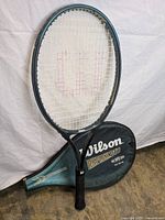 Wilson Reflex DTB tennis racquet leaning against its matching carrying bag, racquet shows nylon strings with Wilson 'W' logo