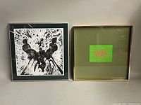 Shows both framed prints side by side, one with black and white figures print and one green with red dots print, illustrating frame wear and colors