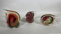 Set of three blown glass fish sculptures shown side by side on a white background, highlighting vibrant swirl colors inside clear glass