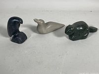 Three soapstone animal carvings on a white surface including perched eagle, loon, and beaver.