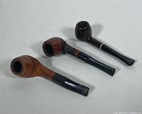 Three vintage tobacco pipes shown from an angled view revealing shaping and condition of bowls and stems.