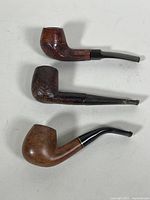 Three vintage tobacco pipes placed flat against white background showing different wood finishes and stem styles.
