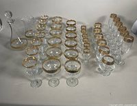 Full set of glassware displayed, showing decanters, water pitcher, and rows of stemware glasses with gold rim detailing.