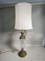 Full lamp showing brass ornate base with clear textured glass midsection and fabric lampshade.