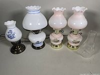 Four vintage electric milk glass hurricane table lamps on display showing various designs and bases