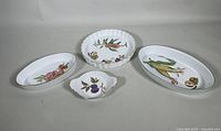 Four porcelain Royal Worcester EVESHAM dishes arranged together showing variety of shapes and painted fruit and floral designs.