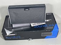 BOSE SoundLink speaker placed on top of its original black and blue box showing brand and model details. Visible wear on box edges.