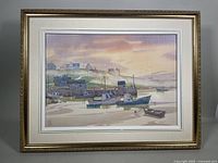 Framed oil painting of a coastal village scene with boats and houses, in a gold decorative frame with matte border.