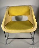 Front angled view of the armchair showing yellow upholstery, molded plastic cream shell, and chrome base.