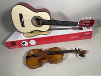 Violin and guitar displayed together with guitar resting on its original box.