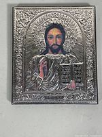 Full frontal view of the silver religious icon plaque showing Jesus Christ with detailed embossed silver border and painted face and book.