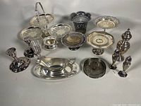 Full collection of vintage silver plated servingware including candleholders, trays, and other pieces photographed on gray surface