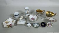 Full display of all eleven miniature bone china items on white surface, showing variation in shape, size, and decoration including vases, teacups, saucers, and dishes.