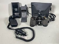 Photo of Motorola flip phone with numeric keypad, display, charging dock, holster case, and coiled car charger cord