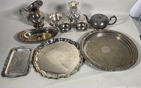 Full set of silver plated servingware including trays, pitcher, teapot, and other pieces arranged on a white surface