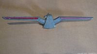 Full view of the 1967 Ford Thunderbird metal emblem showing bird shape and wing details with red accents.