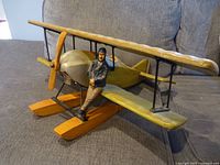 Side view of the wooden biplane airplane décor showing the pilot figurine leaning on the front float with details of the wings and propeller.