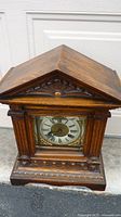 Front view of the antique wooden mantel clock showing carved wooden details and clock face.