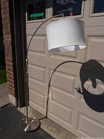 Full view of the arc floor lamp showing the metal arc arm, round base, and white fabric lampshade in natural light.