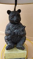 Close-up of the black bear figurine holding a fish on the base of the lamp. Sculpture shows detailed texture and colors for rustic decor style.