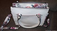 Front view of white leather purse with floral strap and Celine Dion logo