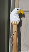 Close-up photo of the carved and painted eagle head at the top of the wooden walking stick, showing detailed feathers and beak.