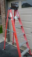 Front-side angle view of the red fibreglass step ladder showing the wide silver steps and black top cap, placed outdoors.