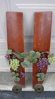 Full view of two oak barrel stave candle holders with metal grape and vine decorations against a door background.