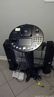 Front view of Singing Machine ISM1030BT karaoke system with main unit on stand, two black speakers on each side, microphones, power cords and manual visible below.