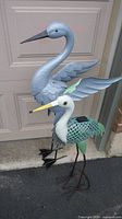 Both metal bird lawn ornaments together showing size difference and color repainted finishes