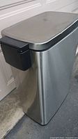 Side view of stainless steel trash can with black plastic handle on side and rectangular lid.
