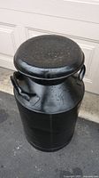 Full view of the black metal milk can showing shape, height, and lid