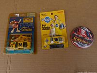Two Ken Schrader NASCAR diecast cars and one collectible tin sealed in original packaging displayed on cardboard.
