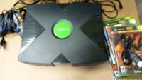 Top view of the original Xbox console with green logo, some cables and game cases on the side.