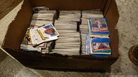 Photo showing a full cardboard box filled with stacked sports cards, mostly hockey cards with some baseball cards evident by photos of players in baseball uniforms.