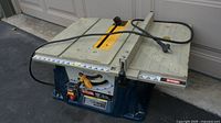 Ryobi 10" table saw angled view with power cord draped over tabletop showing general condition and power switch.