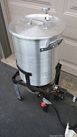 Full view of outdoor aluminum turkey fryer pot and lid on metal stand.