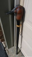 Full view of the wooden walking cane with duck head handle showing the carved and painted duck head and black shaft with yellow rings.