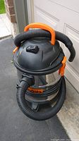 Front angled view of Kubota wet/dry vacuum showing stainless steel body, orange handle, and black hose coiled on top.