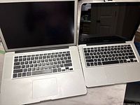 Two Apple MacBooks open, keyboard and screen shown, both inactive, no chargers present